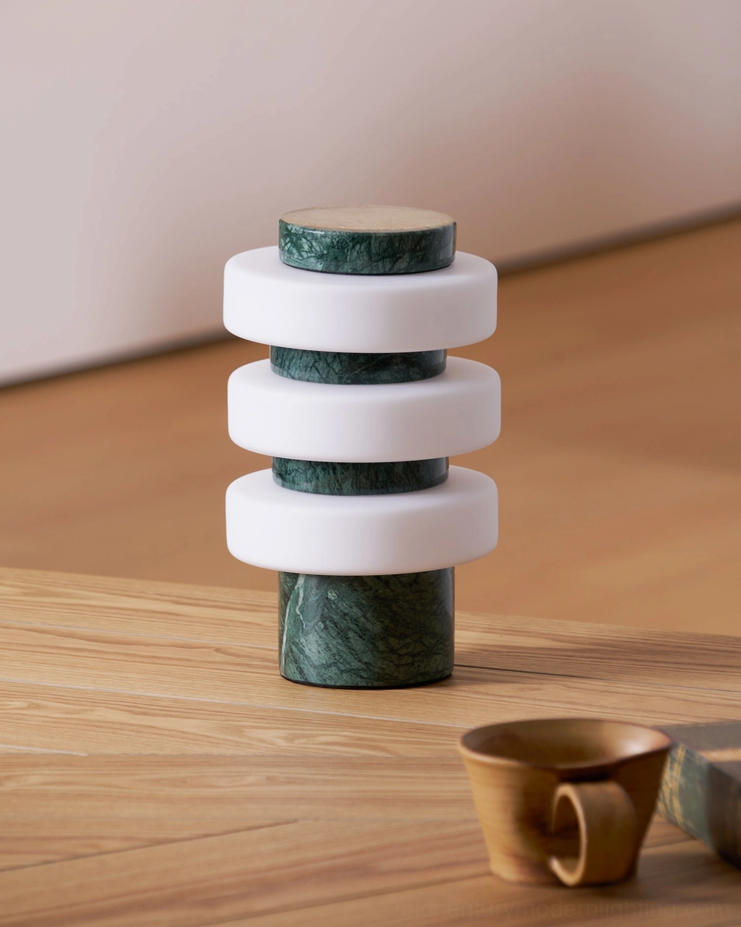 Corba sculptural table lamp with dark green marble base and stacked glass discs on wooden table with ceramic decor