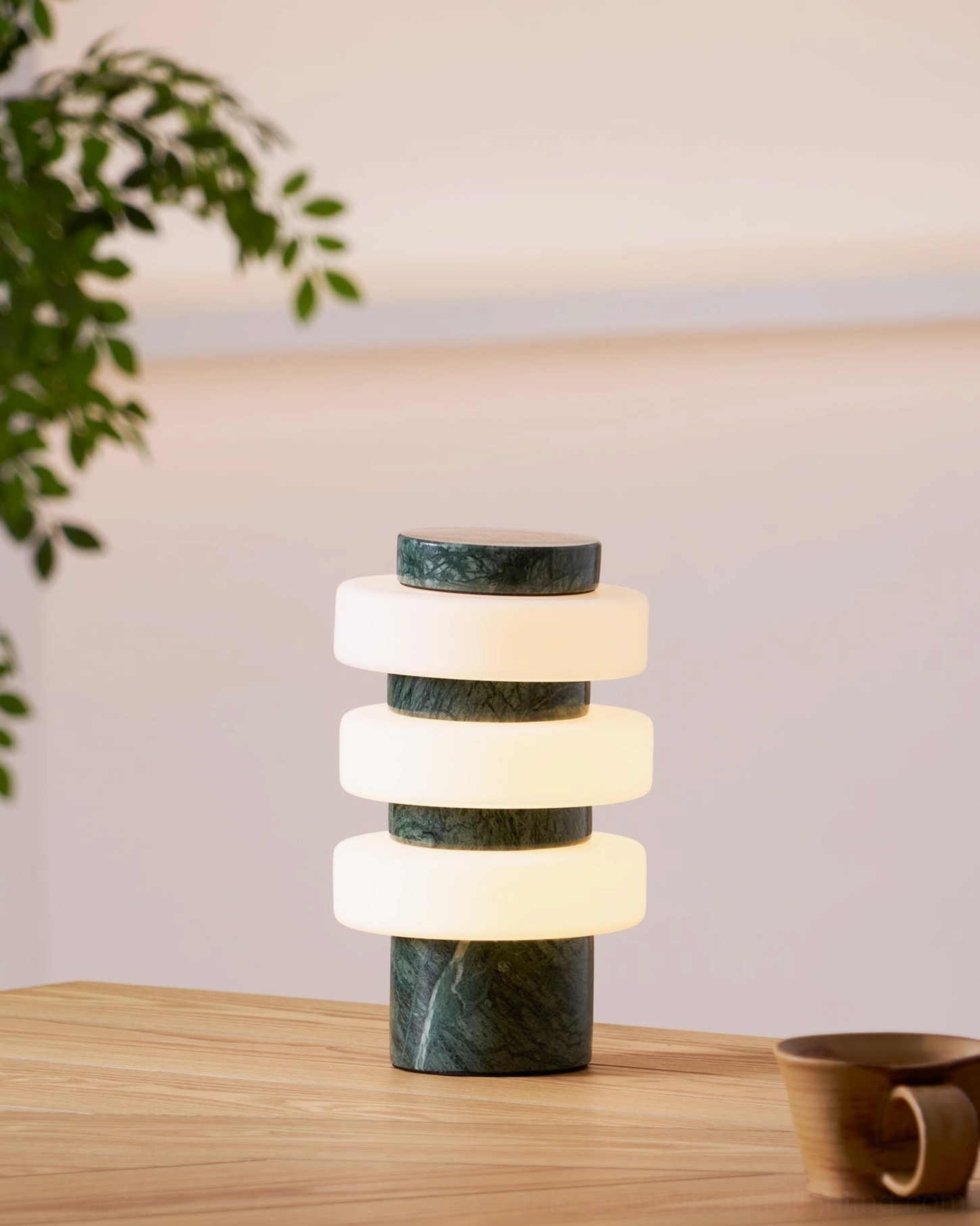 Corba table lamp with green marble base and warm frosted glass layers on table with ceramic cup and plant
