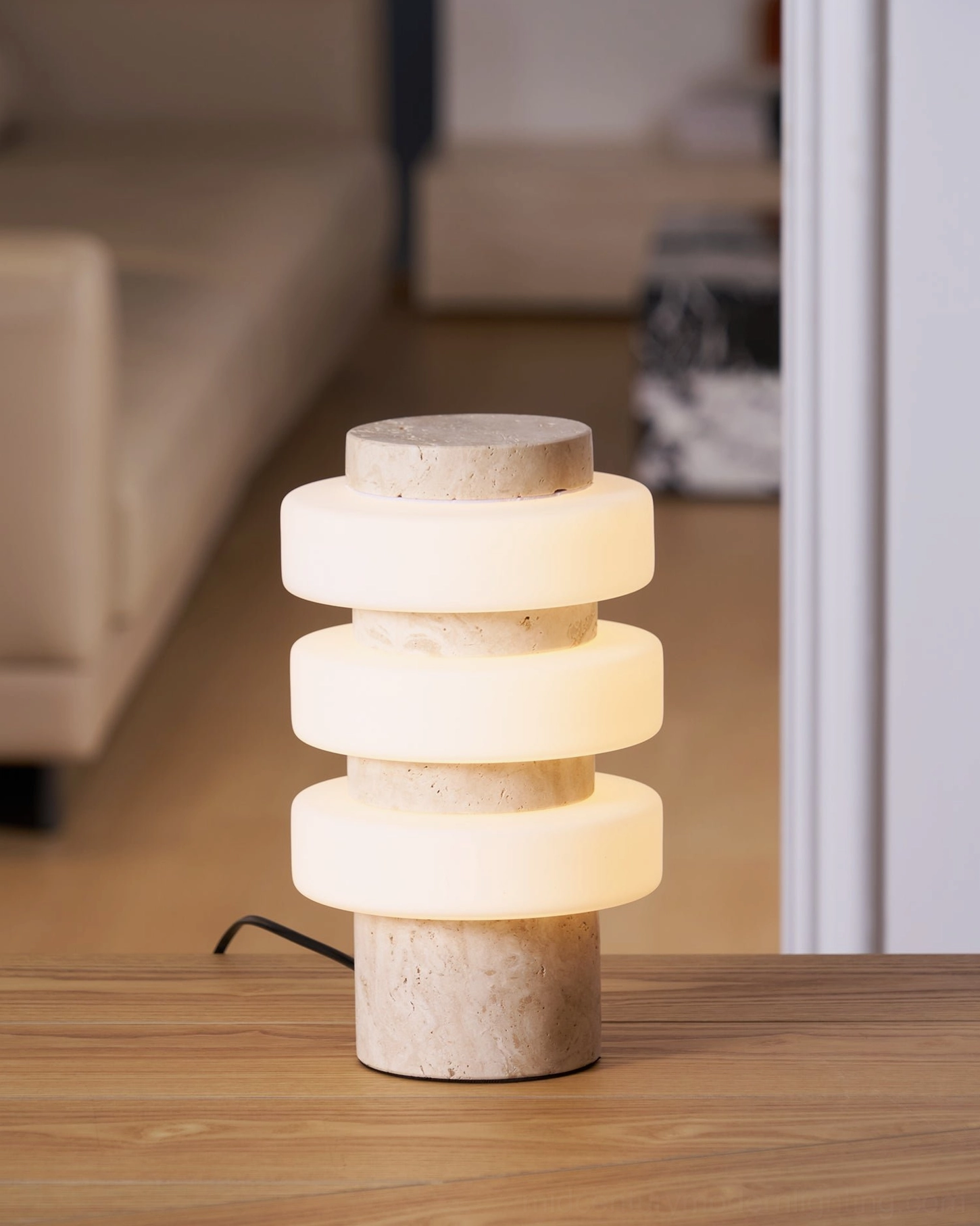 Corba table lamp with beige travertine base positioned on interior wooden surface with wall shelf decor