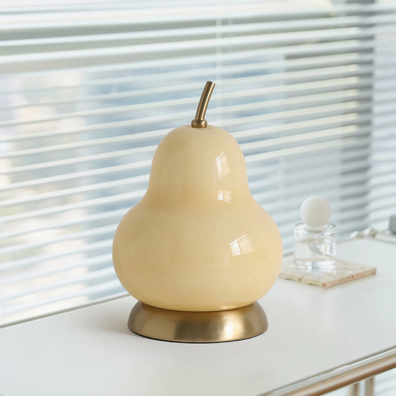 Modern pear glass rechargeable table lamp displayed on windowsill with blinds, showing three-quarter angle with warm ambient light