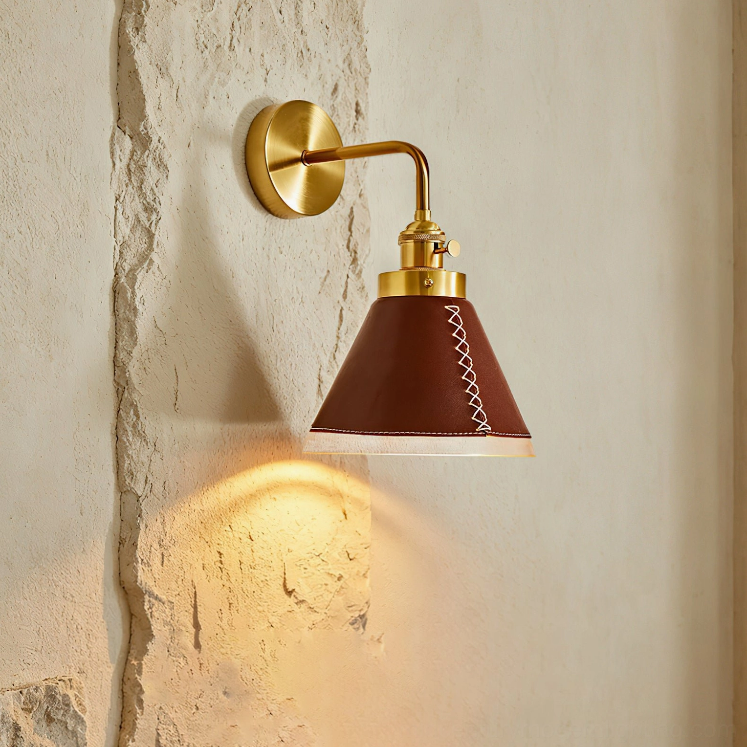 Cordoba wall sconce illuminated side angle showing leather diffuser with white stitching detail against plaster wall