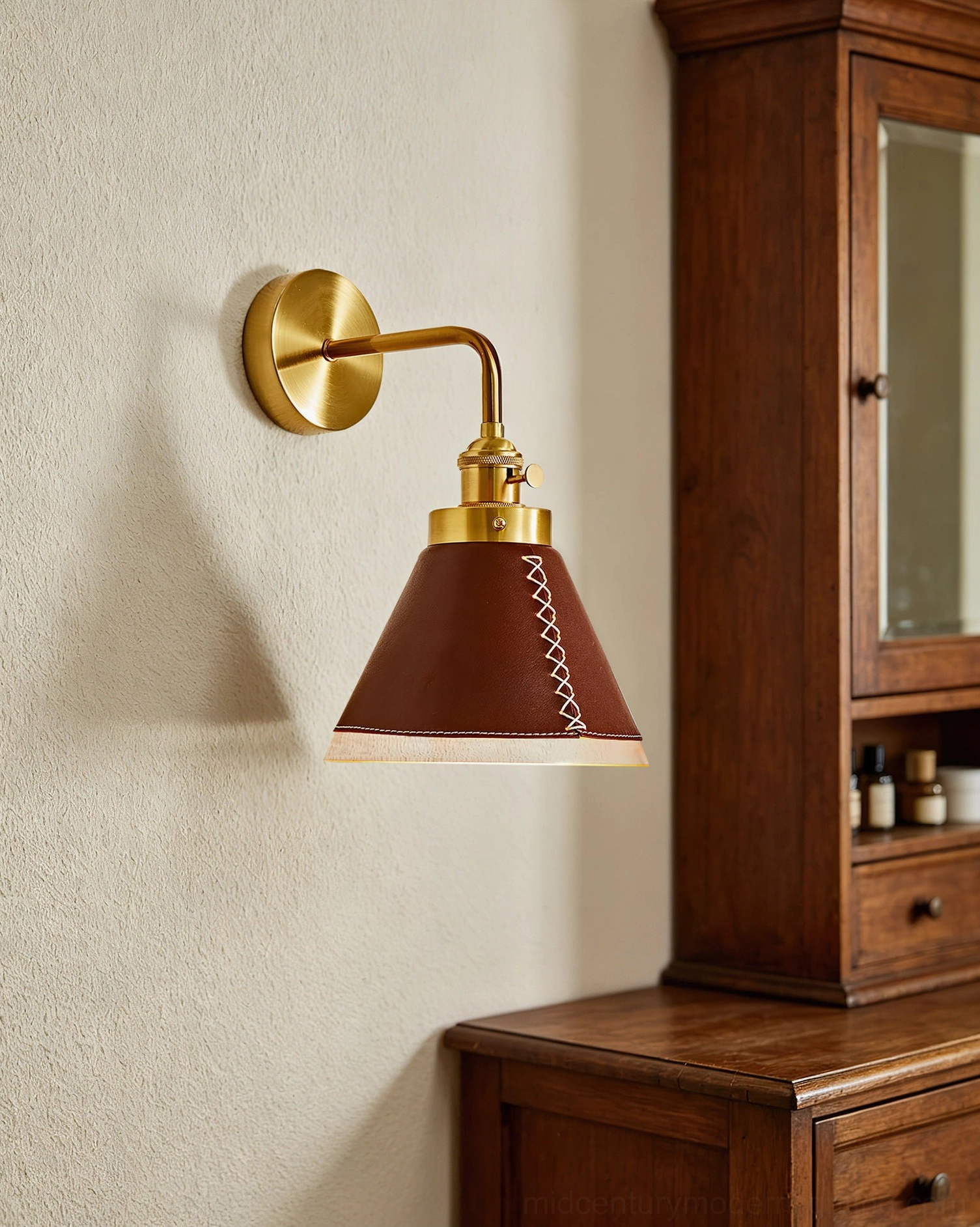 Cordoba wall sconce mounted above wooden vanity cabinet with brass finish and hand-tailored leather shade