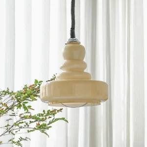 Cream colored gourd pendant light hanging in farmhouse style interior with sheer white curtains and green foliage background