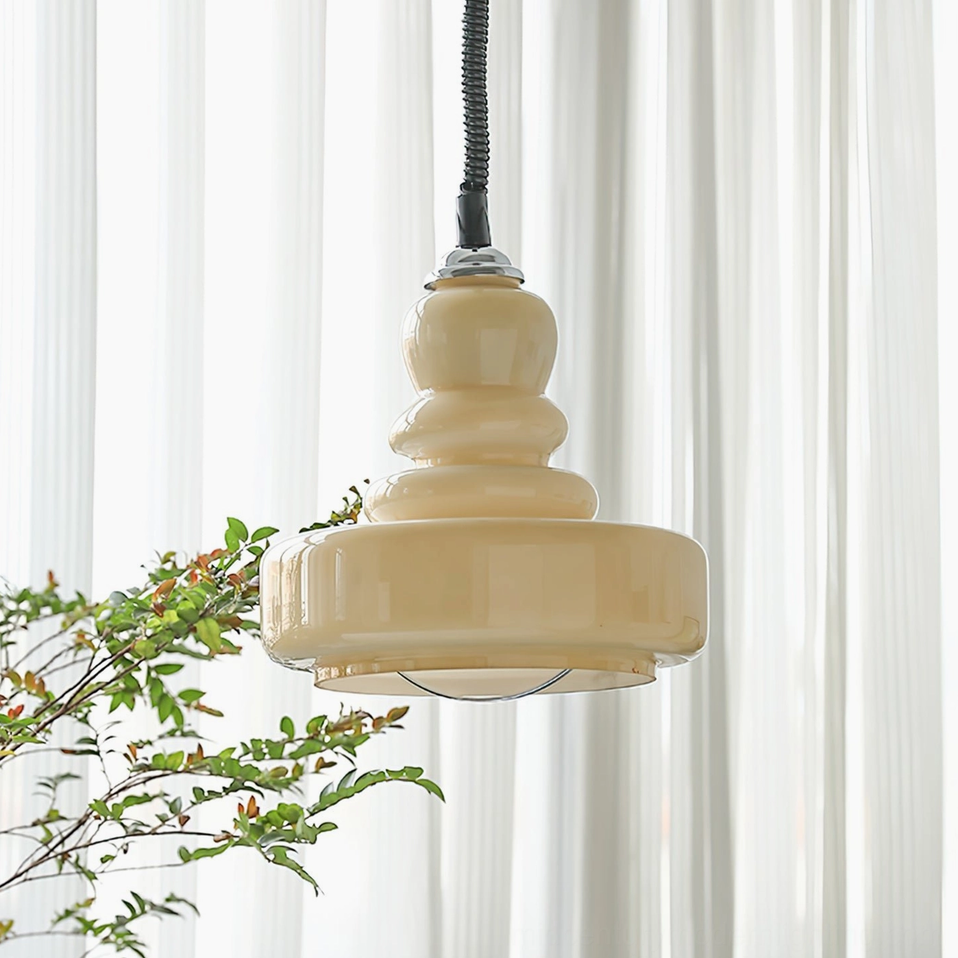 Cream colored gourd pendant light hanging in farmhouse style interior with sheer white curtains and green foliage background
