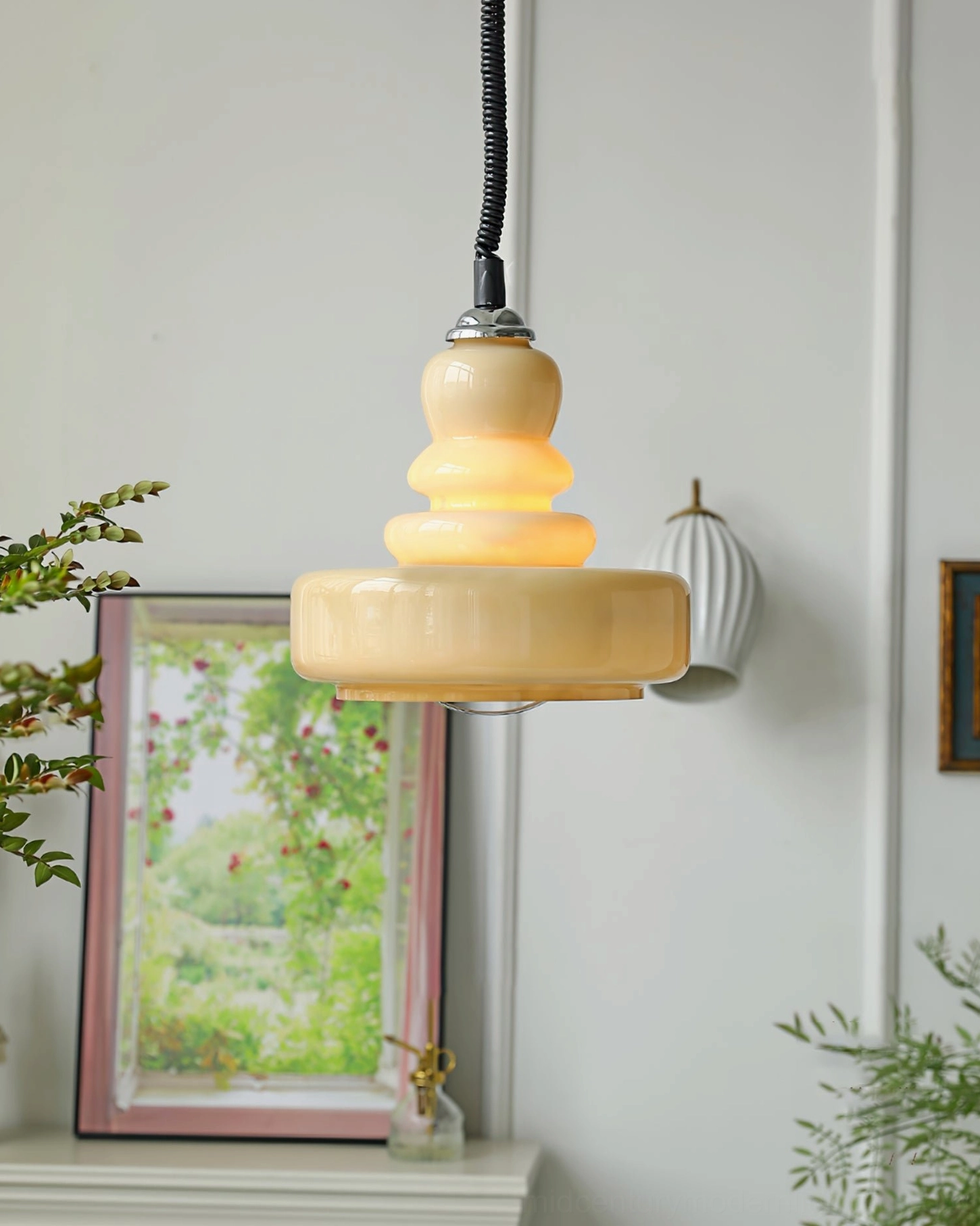 Cream gourd pendant light hanging beside living room mantel with beige stacked glass shade and wall artwork backdrop