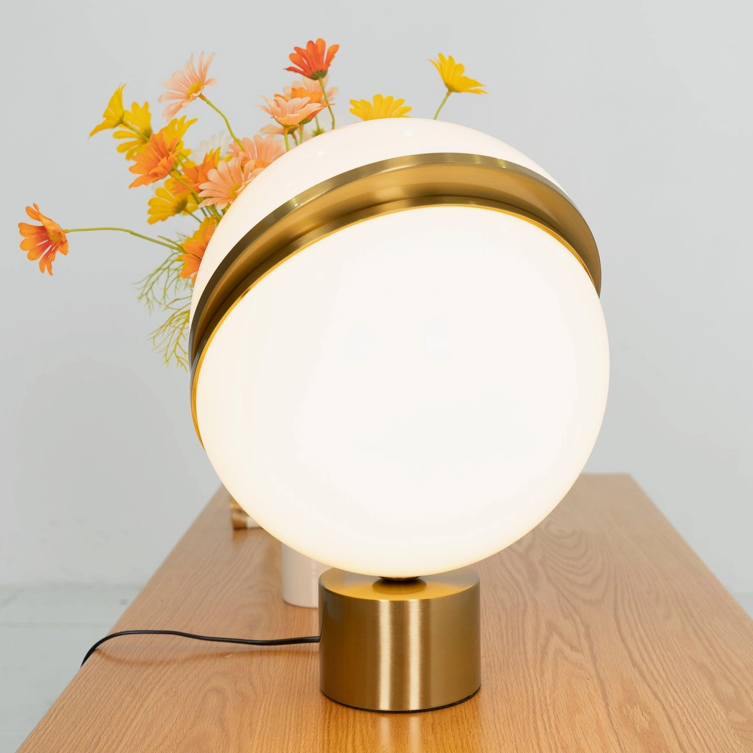 Close-up front oblique view of lit Crescent Sphere Table Light on wooden table with floral arrangements
