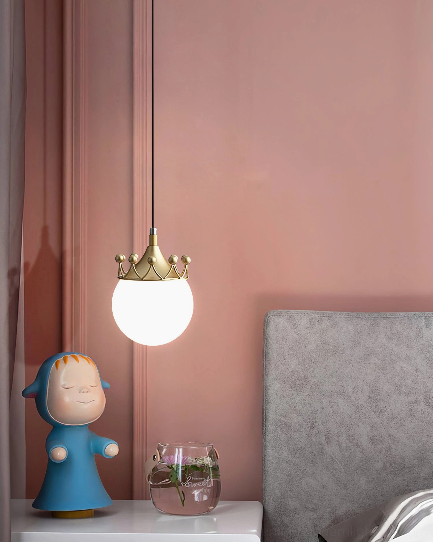 Crown-topped globe pendant light above pink wall bedroom nook with decorative blue cartoon figurine on nightstand