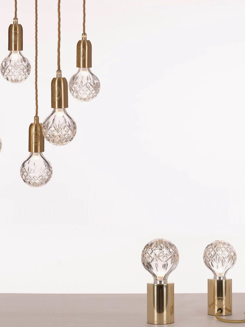 Pair of matching crystal bulb table lamps with brass bases and exposed power cords on desktop
