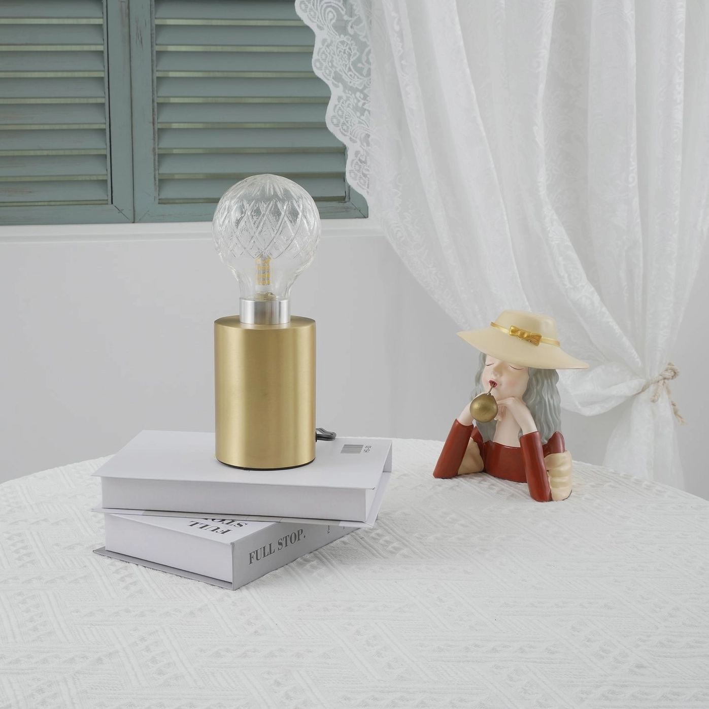 Hand-cut crystal bulb table lamp with brass holder on white lace table with vintage doll and window