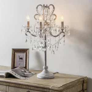 Crystal candelabra table lamp with lit candle bulbs and crystal pendant decorations styled on vintage nightstand with framed art and magazine, retro white distressed finish