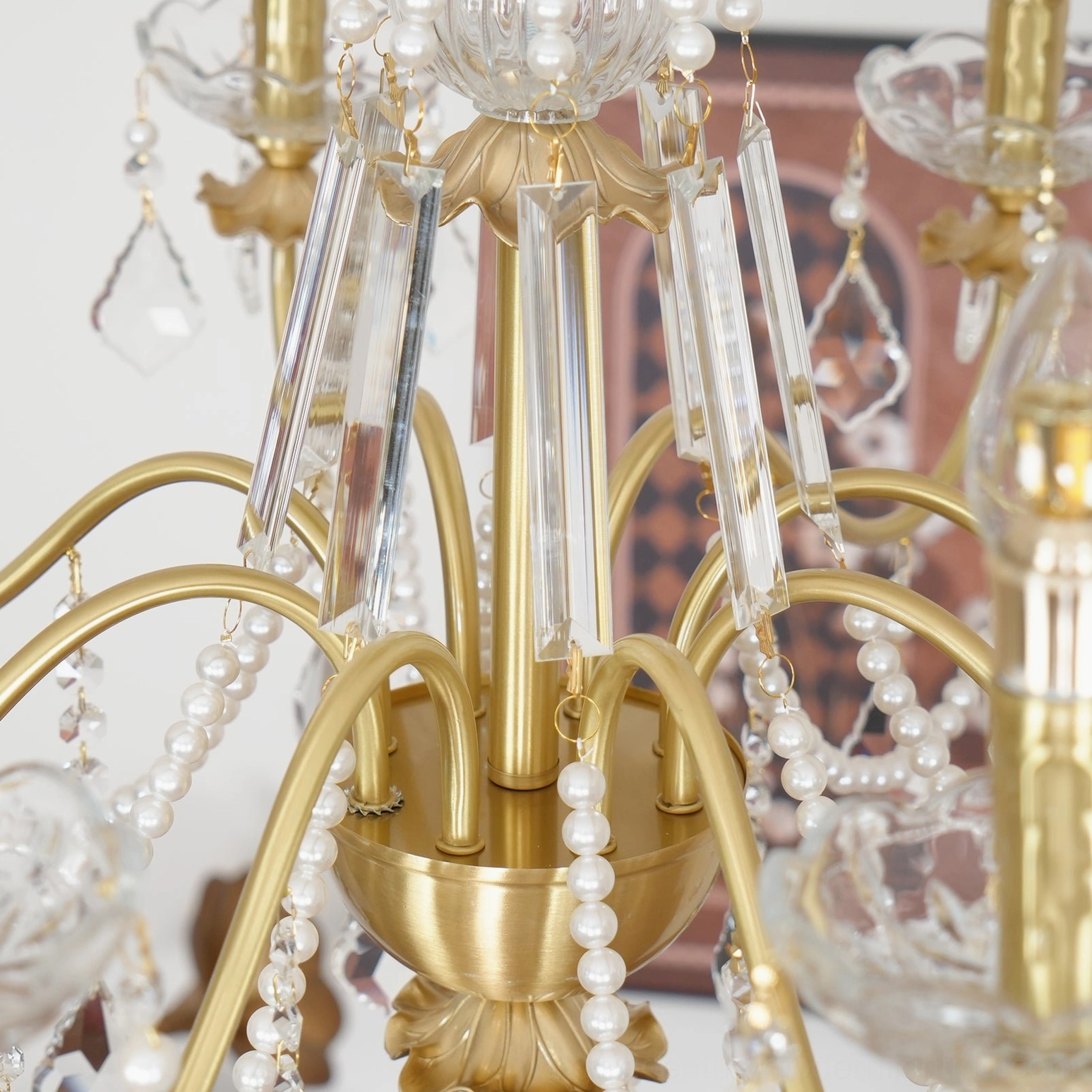 Macro close-up detail of brass chandelier arms, clear crystal strands, and pearl string accents