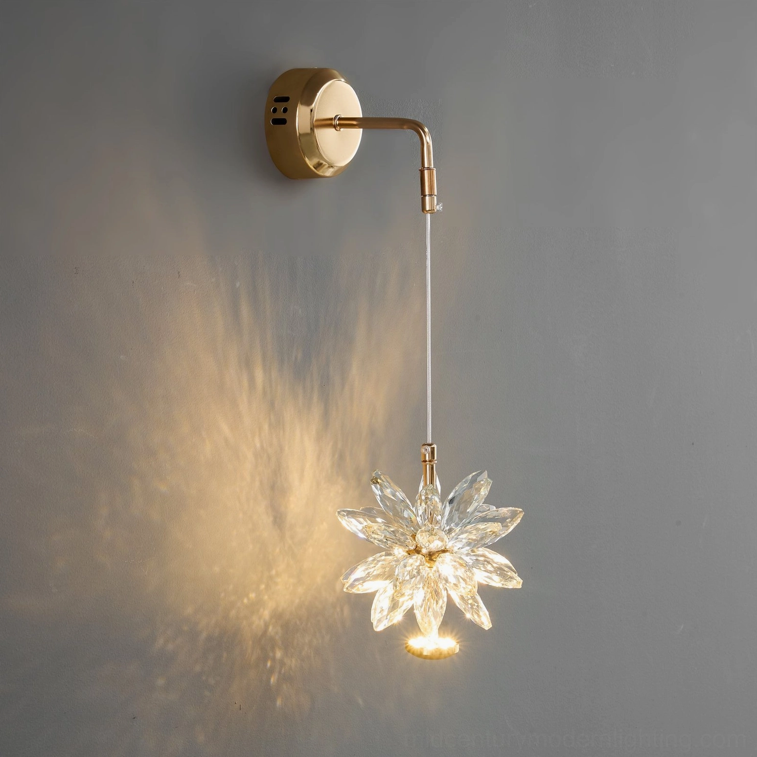 Crystal flower wall sconce illuminated on gray interior wall, highlighting the dramatic warm light diffusion and starburst glow