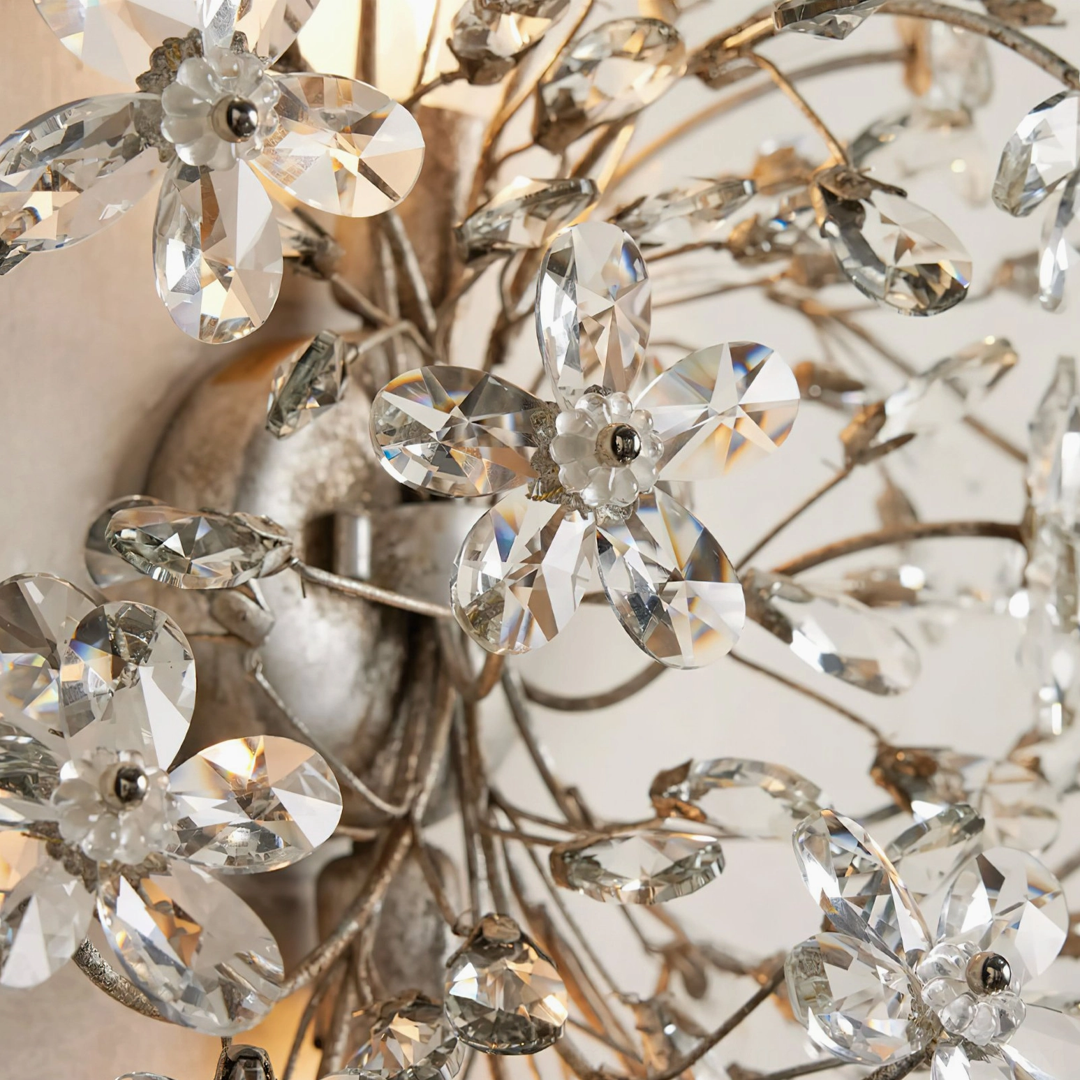 Macro close-up of silver crystal wall lamp showing detailed faceted crystal flowers and polished metal branch structure