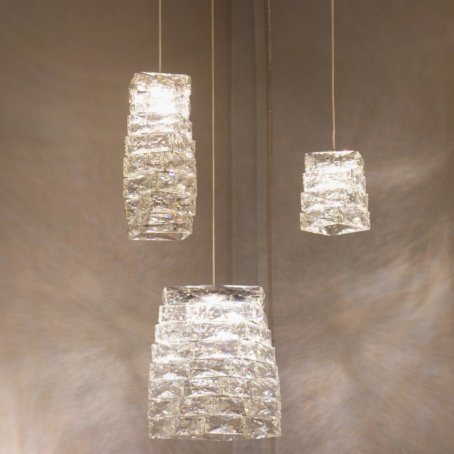 Three different sized faceted crystal pendant lamps arranged together showing size variations with soft warm glow