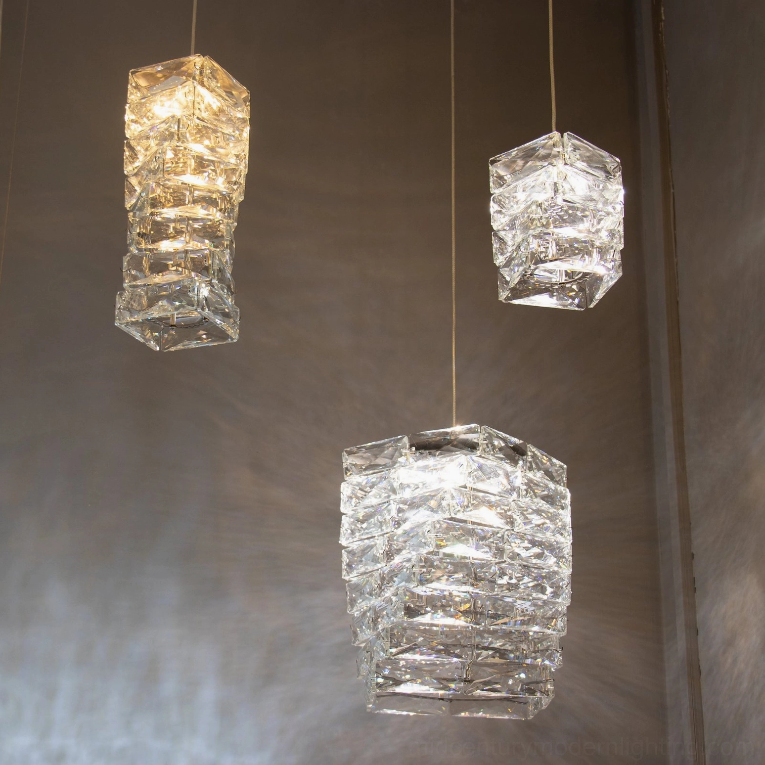 Multiple faceted crystal pendant shades in varying shapes arranged on neutral wall background showing crystal texture detail