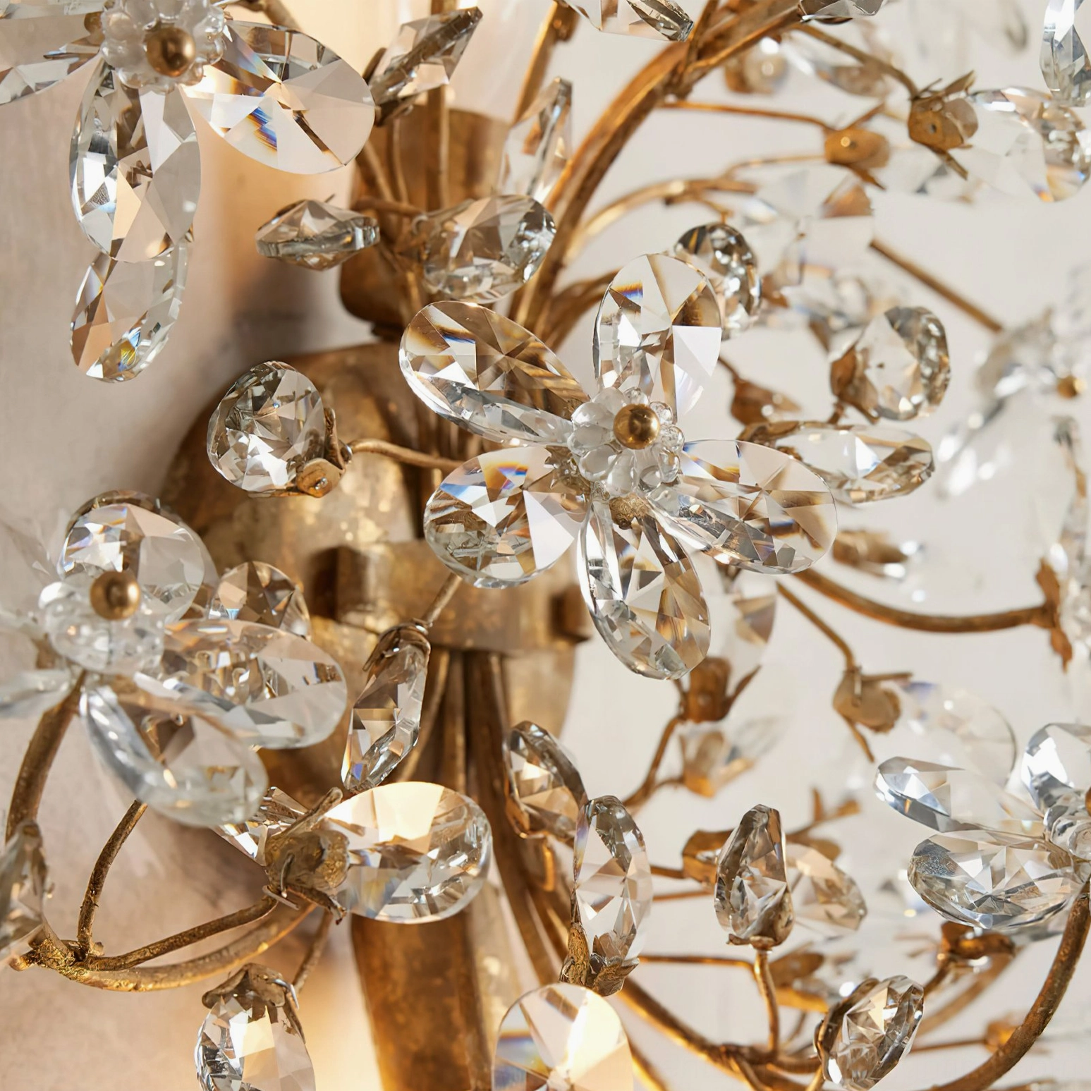 Extreme close-up of gold crystal wall lamp detail, showing refractive faceted crystal petals and polished metal hardware craftsmanship