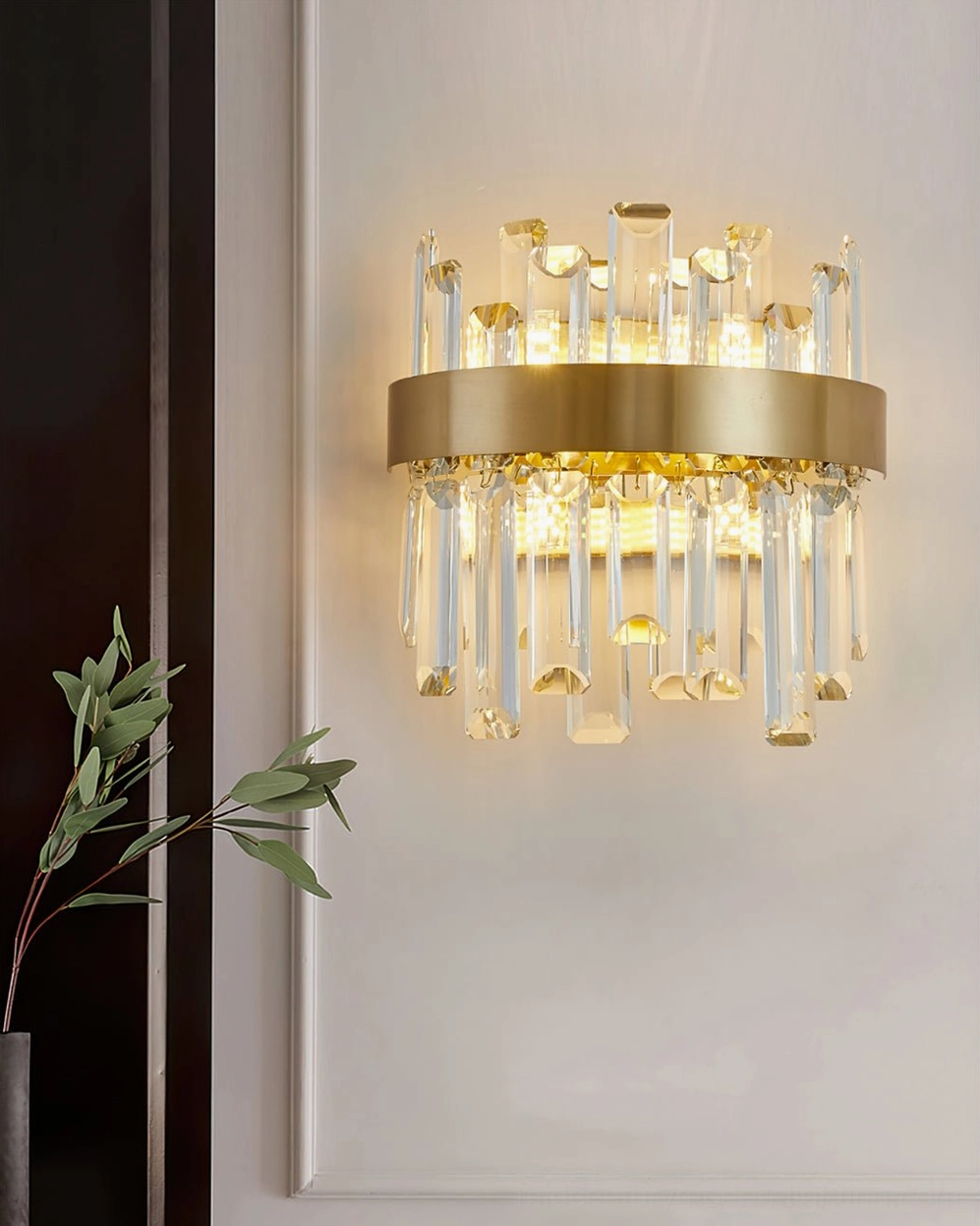 Modern crystal wall fixture in luxury hallway with dark wood trim, paired with green botanical decor and glowing warm ambiance