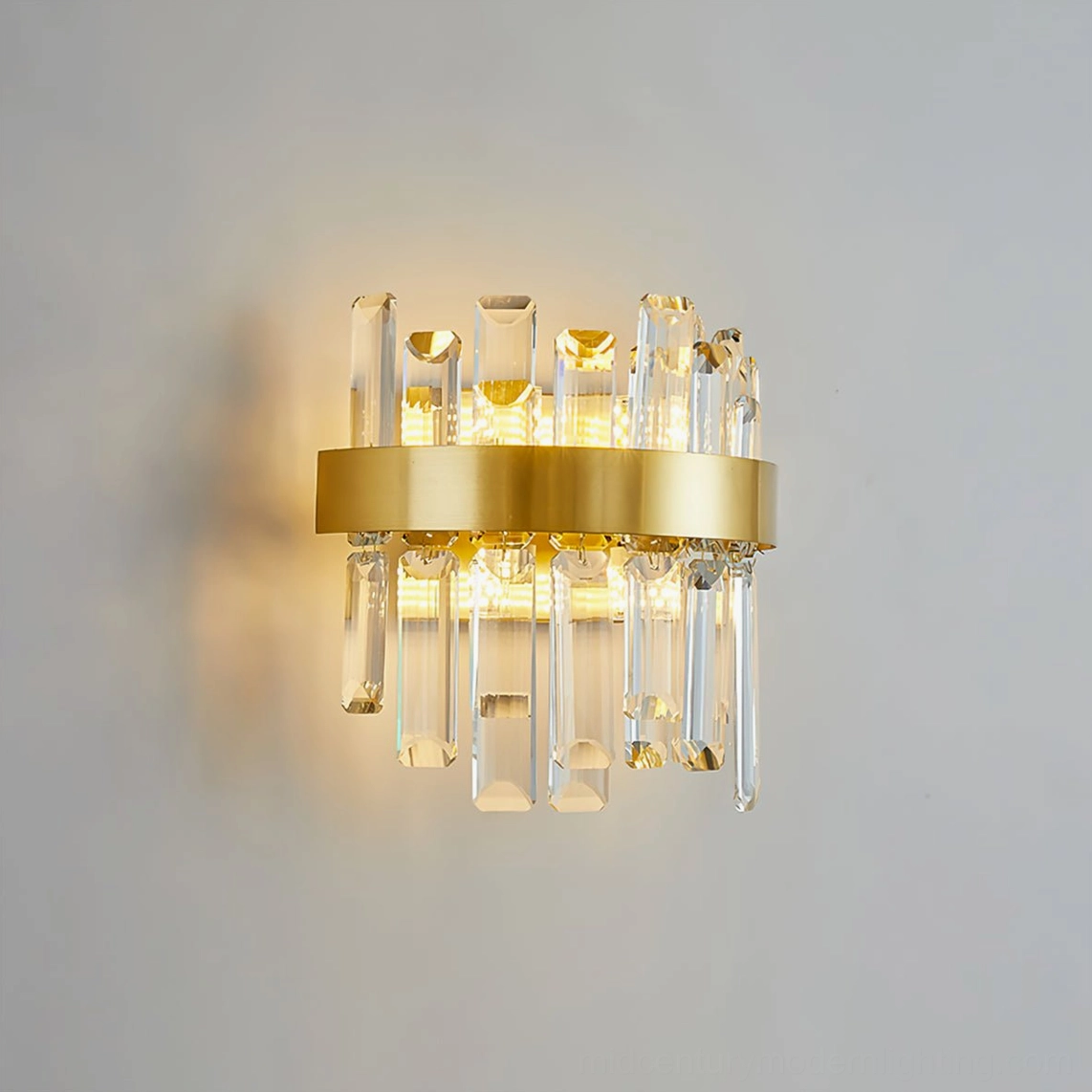 Crystal statement wall lamp mounted on light gray interior wall, illuminated with warm yellow light creating elegant shadow patterns