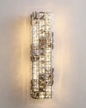 Close-up detail of faceted crystal wall lamp showing light refraction and warm LED glow against grey wall