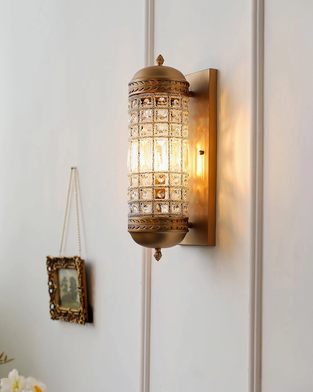 Lit wall sconce with warm glowing light and brass base on white paneled wall