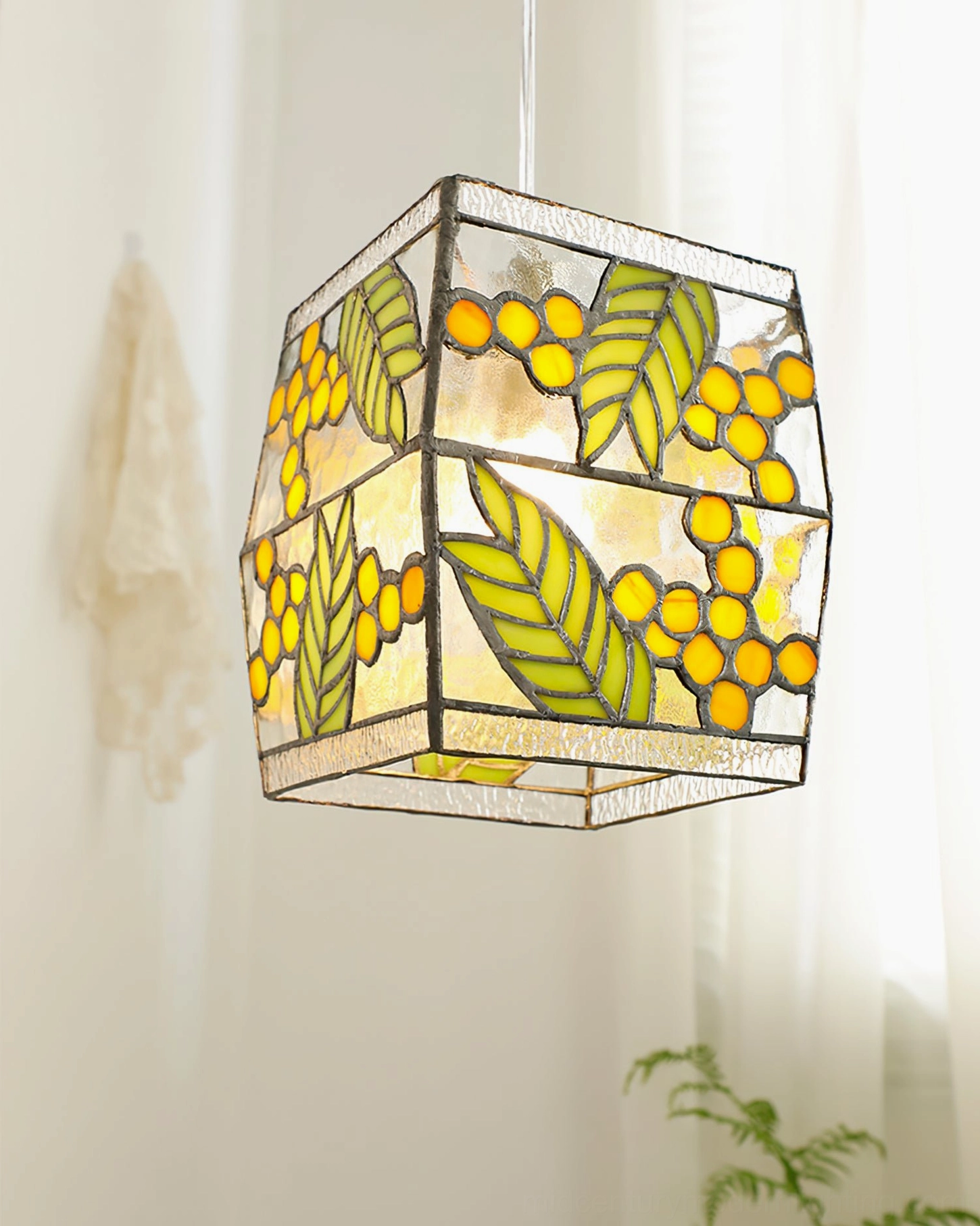 Side-angle view of stained glass cube pendant light in minimalist bright space, leaf and berry botanical details clearly visible