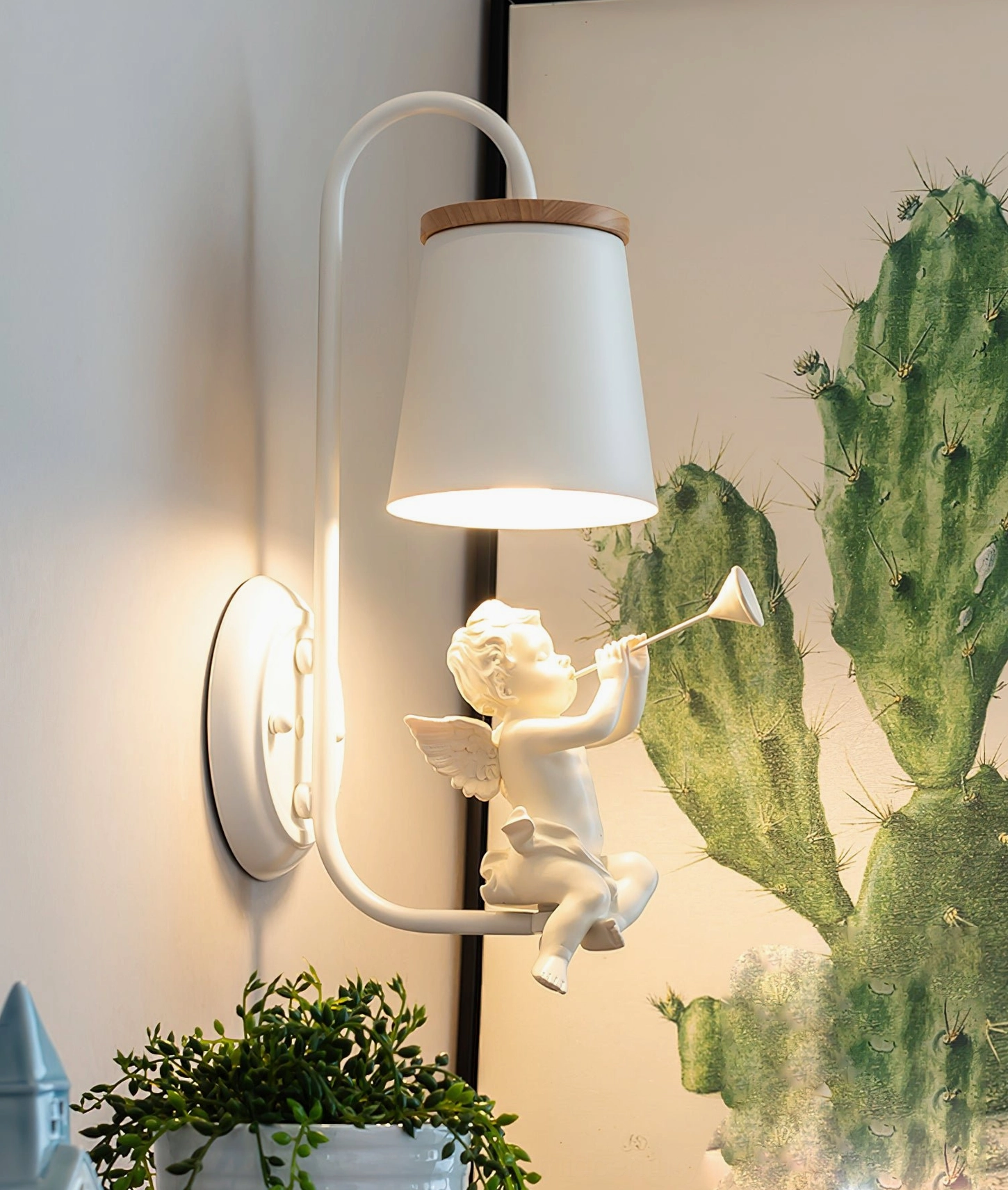 Nordic-style angel wall lamp with cherub figure mounted on home wall with cactus art and potted plant decor