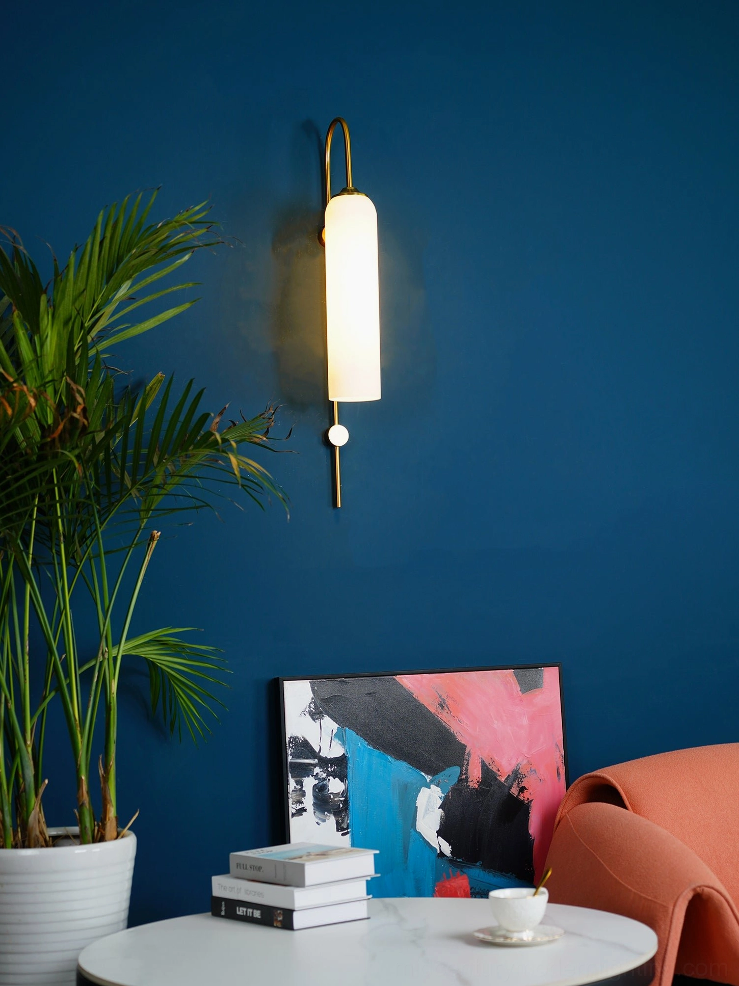 Elegant glass wall sconce with curved top metal arm and hanging spherical detail against dark blue accent wall