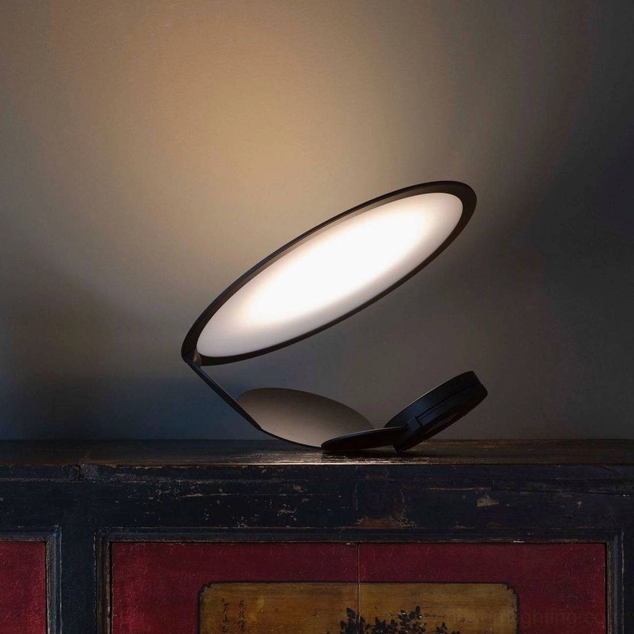 Modern geometric table lamp with two folded circular panels creating warm ambient lighting on vintage wooden cabinet