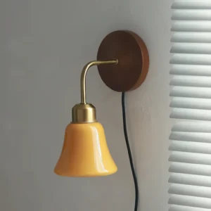 Daphne Pastel Wall Sconce three-quarter view installed on white louver blinds interior, displaying warm brass hardware and natural wood base with black power cord