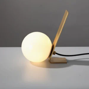 Daphne table lamp low angle perspective showing lit frosted glass orb and brass arm detail