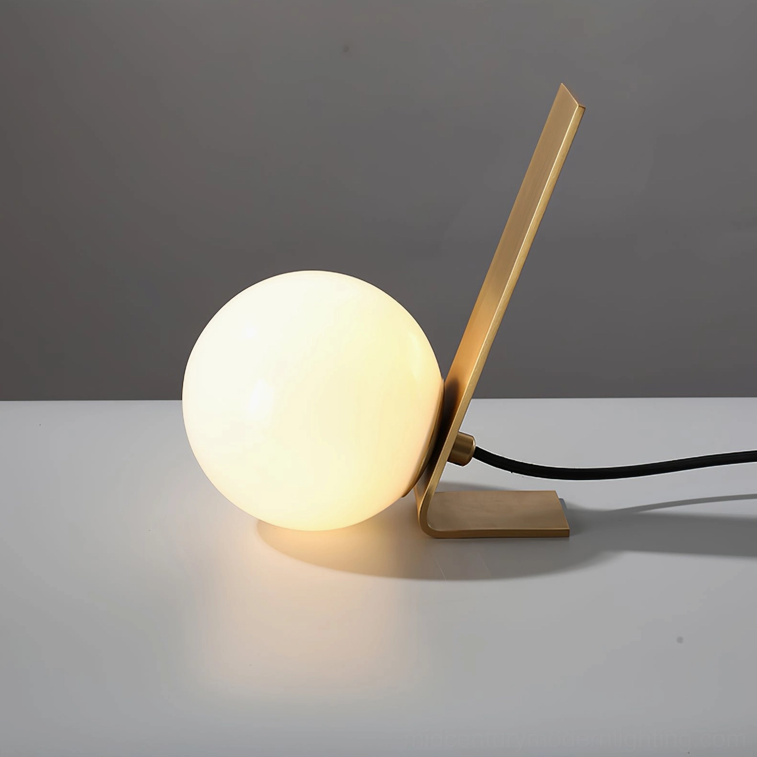 Daphne table lamp low angle perspective showing lit frosted glass orb and brass arm detail