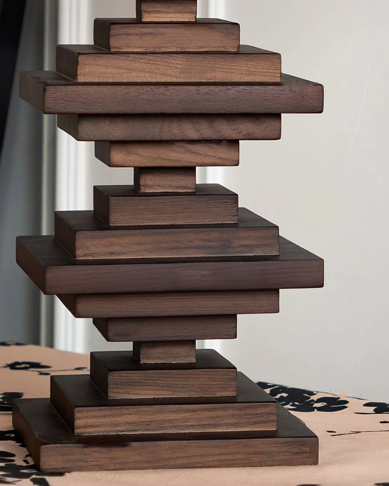 Stacked wood tower lamp with dark finish displayed on dark wood surface with dried foliage accent