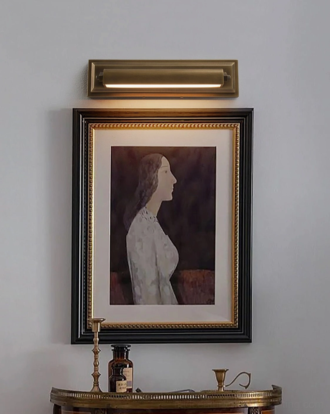Davenport sconce mounted above antique console table and framed portrait artwork, gallery wall styling with warm brass lighting