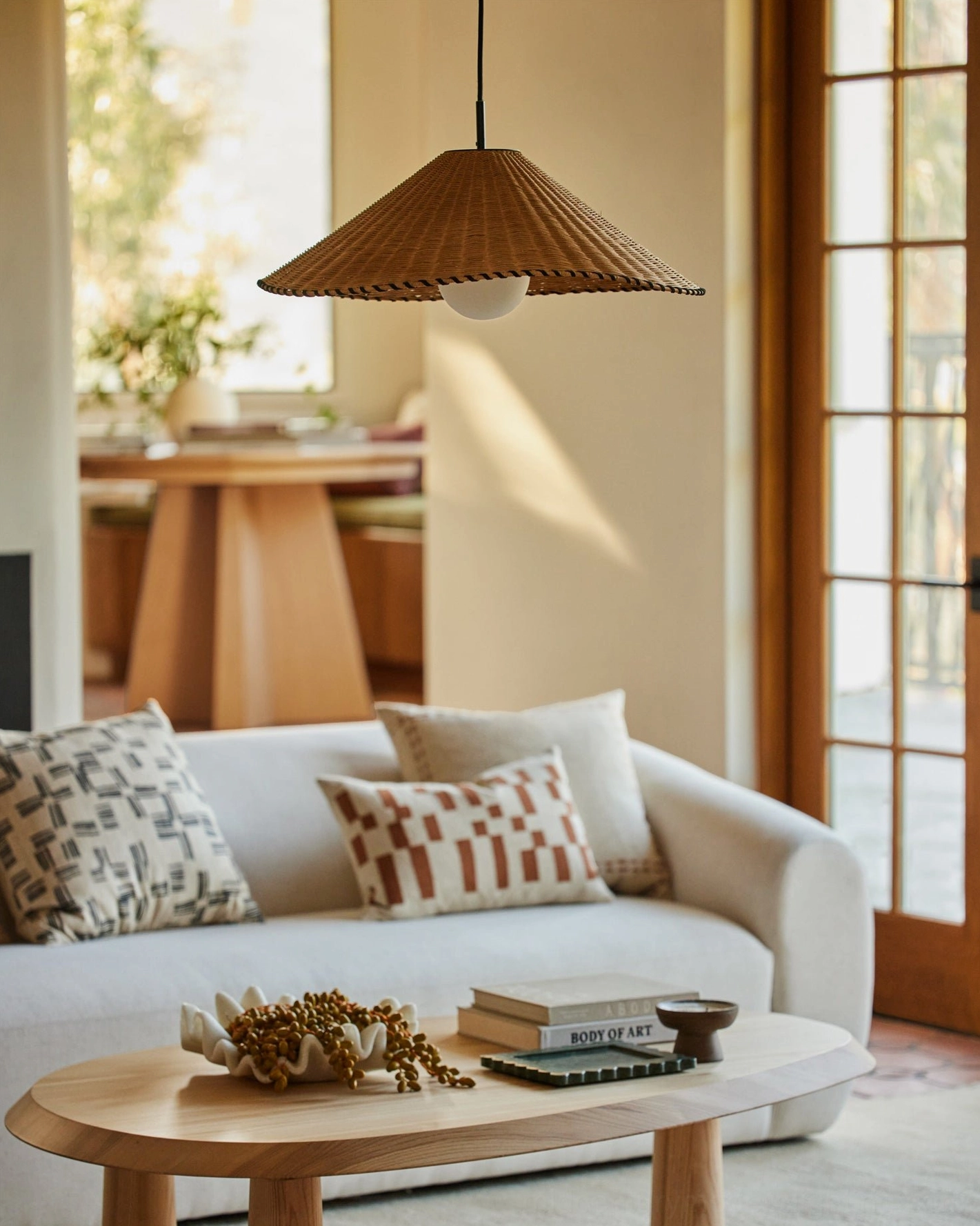 Single hand-woven rattan pendant light in cozy neutral living room, brown conical shade with soft downward glow