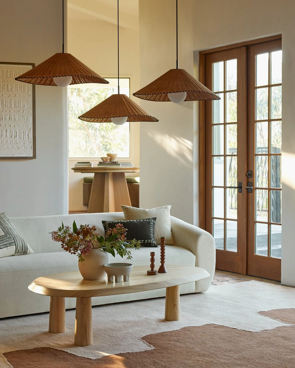 Three hand-woven rattan pendant lights in bright boho living room, matching conical shades with warm ambient lighting