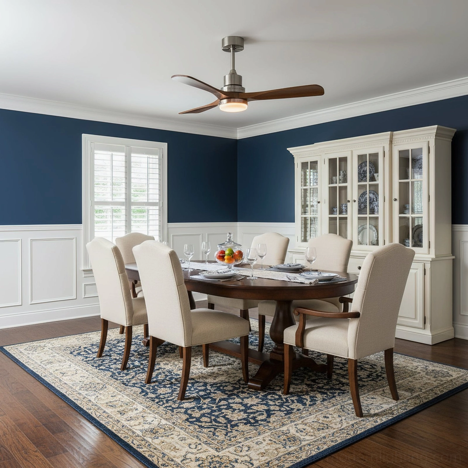 Contemporary DC motor ceiling fan light in navy blue dining room interior, eye-level view showing dark wainscoted walls and glass-front cabinet