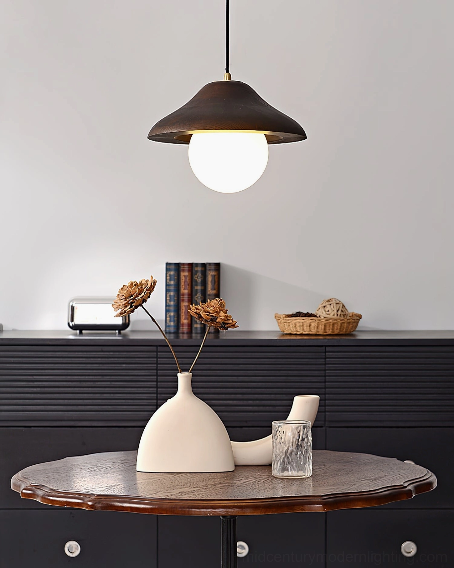 Delano pendant with lit frosted white bulb suspended over dining table with dark wood sideboard, creating warm intimate ambiance