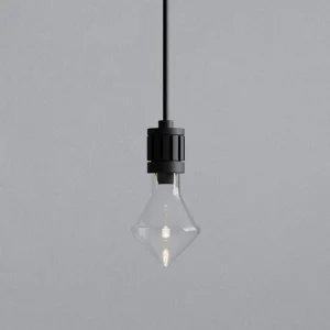 Close-up detail of modern diamond glass pendant lamp showing clear rhombus shade and black metal socket against textured wall