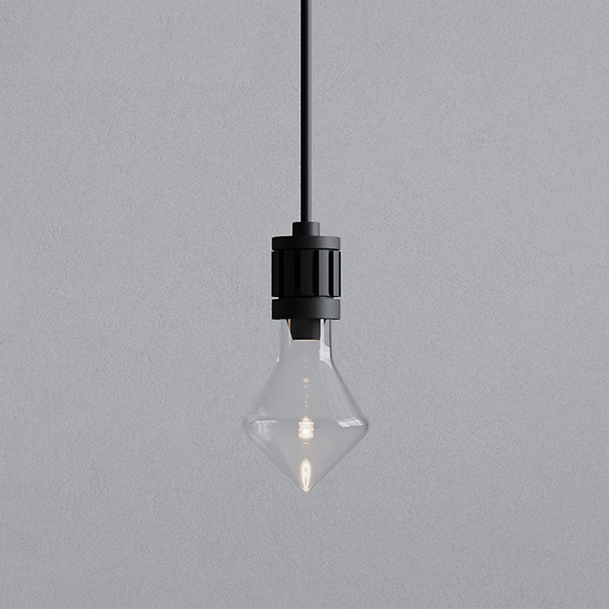 Close-up detail of modern diamond glass pendant lamp showing clear rhombus shade and black metal socket against textured wall