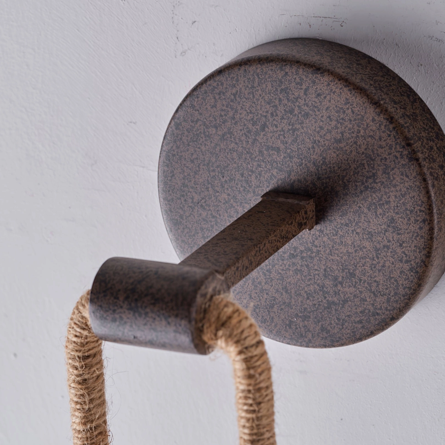 Dillon wall lamp mounting bracket detail showing speckled dark brown metal and hemp rope connection joint