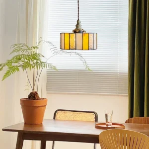 Mid-century modern stained glass drum pendant lamp in dining nook with potted fern and warm ambient lighting creating cozy dining atmosphere