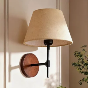 Dodie wall sconce mounted in modern bedroom with wainscoting, showing warm ambient lighting and three-quarter perspective