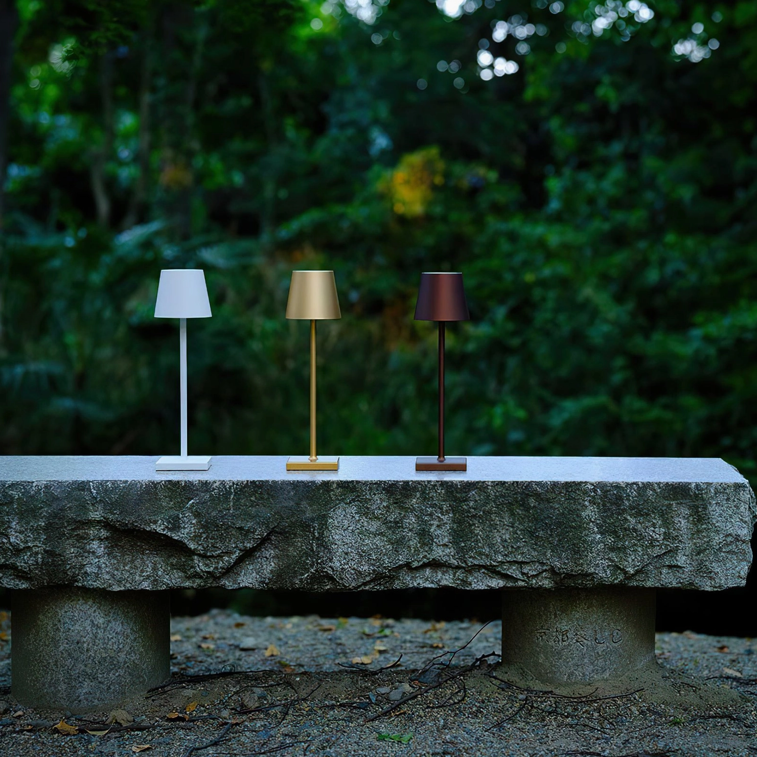 Three Doku portable table lamps in white, gold and black finishes on outdoor garden patio bench