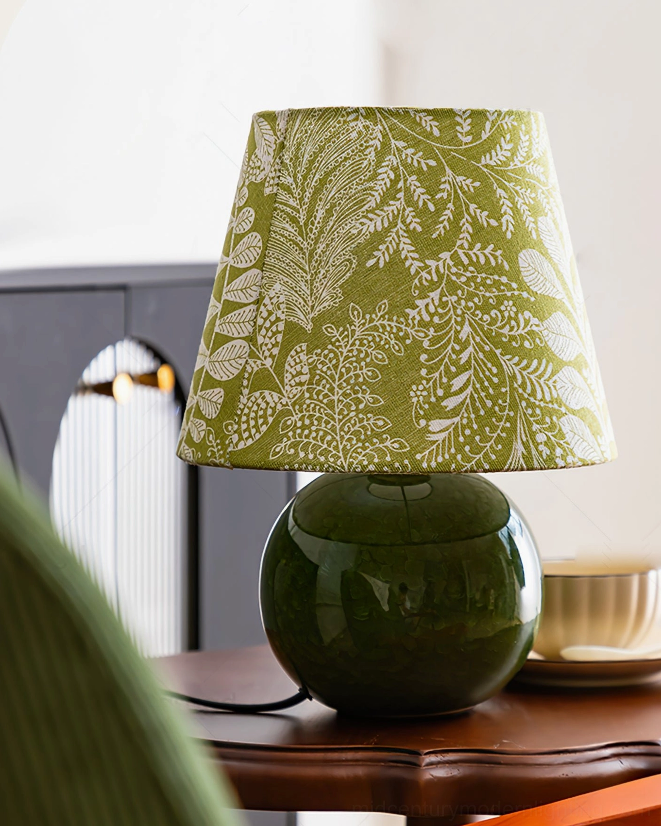 Dolly table lamp side view on retro wooden side table, deep green ceramic with leaf pattern shade
