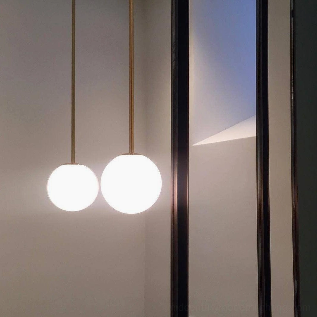 Double brass globe pendant lights displayed through glass partition in contemporary interior
