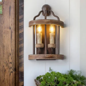 Double candle wall lamp installed in farmhouse entryway with wooden door and potted plants, warm ambient lighting