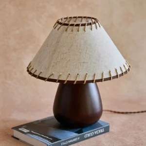 Close-up of Douglas walnut wood base and linen shade with whipstitch border detail, styled on hardcover book