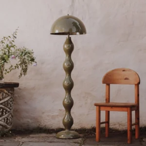 Drop floor lamp in glossy olive green finish with twisted gourd-style pole displayed in rustic courtyard setting with stucco wall backdrop