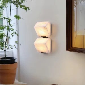 Two-light alabaster wall sconce mounted in contemporary bedroom with warm diffused glow, side view showing depth and translucent stone