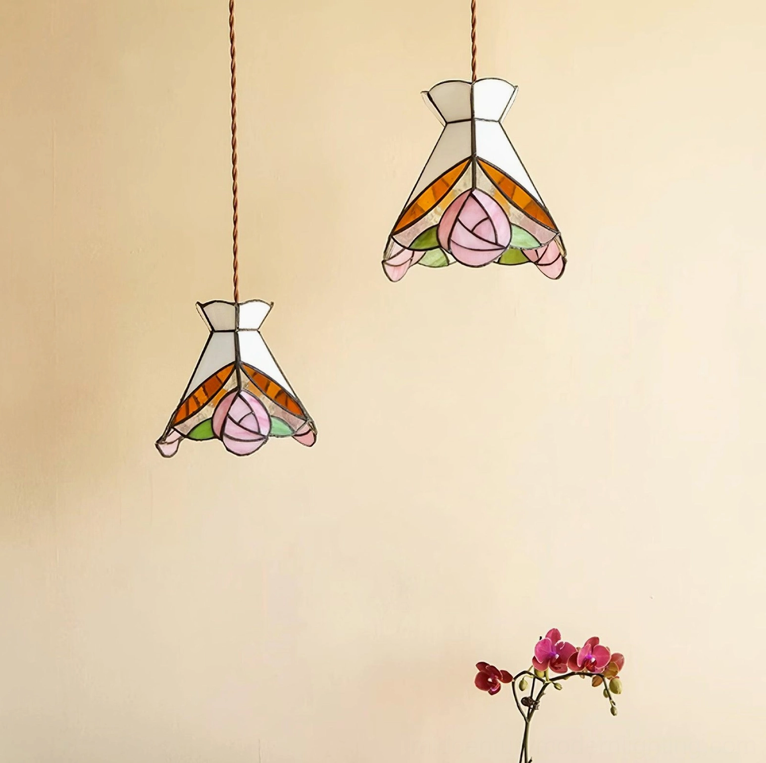 Two Tiffany rose stained glass pendant lights displayed together on warm-toned wall with potted flowers decor